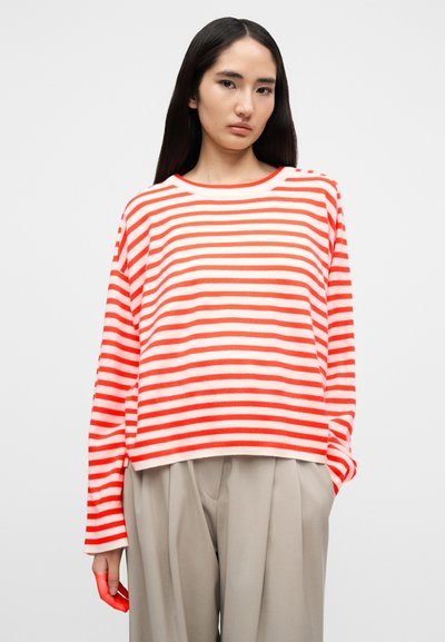 Pull oversize à rayures rouges et blanches avec un col rond et des manches longues, fabriqué en tricot doux. Associé à un pantalon beige.