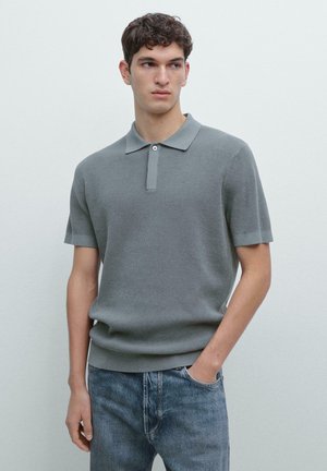 Polo a maniche corte in tessuto grigio chiaro strutturato, con colletto con bottoni e orlo a coste, abbinata a jeans di denim blu.