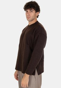 Maglione lungo a maniche ripiegate di colore marrone con una vestibilità comoda e scollo tondo, caratterizzato da un tessuto testurizzato e cuciture delle spalle abbassate.