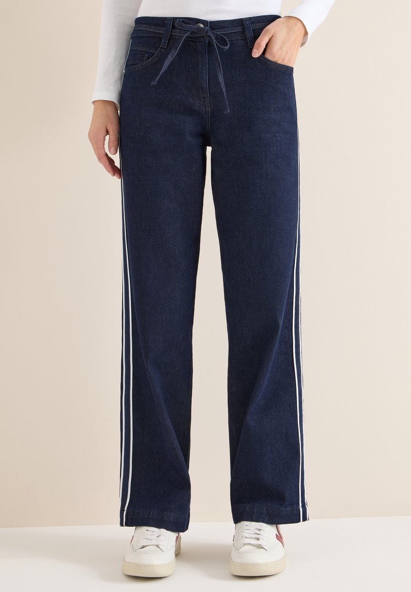 Námořnicky modré džíny s volným střihem, s bílými bočními proužky a pasem se stahovací šňůrkou. Ozdobené předními kapsami.