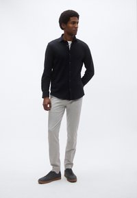 Czarna koszula z długim rękawem zapinana na guziki, szare dopasowane spodnie slim fit oraz ciemne sneakersy z gumowymi podeszwami. Model stoi na jednolitym białym tle.