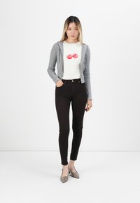 Sivi zip-up dukserica preko bijele majice s grafikom crvenih trešanja, uparena s crnim uskim trapericama i sivim cipelama s oštrim vrhom. Jednostavan dizajn.