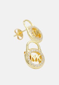 Pendientes en tono dorado con forma de candado, que presentan un logotipo "MK" en el centro y están rodeados por un anillo de piedras preciosas transparentes.
