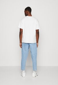 Tricou alb cu mânecă scurtă, croială lejeră. Pantaloni din denim bleu deschis, cu tivuri răsucite, asortați cu adidași albi. Design simplu și funcțional.