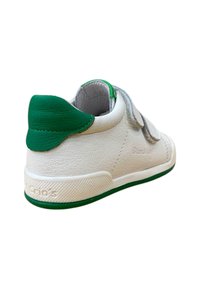 Zapatilla de cuero blanca con acentos verdes, que presenta un cuello acolchado, dos correas de Velcro y una suela de goma texturizada. El logotipo está grabado en el talón.