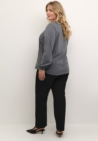 Grey long-sleeve blouse with a smooth texture and relaxed fit, paired with black tailored pants and pointed-toe black heels.