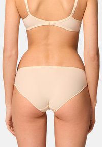 Beige underkläder set med en slät, sömlös textur, justerbara axelband och en hyssochögla stängning på ryggen.