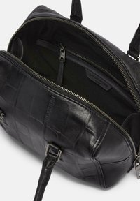 Sac en cuir noir avec une finition texturée, doté d'une fermeture éclair et de poches intérieures. La doublure est en tissu foncé, et le matériel est métallique.