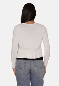 Maglione bianco con un design aderente e dettaglio plissettato sul retro, abbinato a jeans azzurri a vita alta. Texture liscia, scollatura semplice.