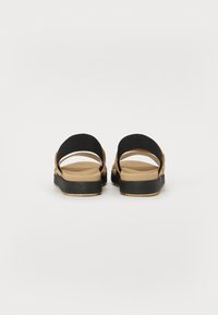 Sorte stoff sandaler med tan fotseng, med to brede justerbare stropper og en tykk svart såle. Minimalistisk design med åpen bak.