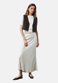 Chaleco marrón a rayas con una blusa blanca de manga corta, combinado con una falda cremosa y fluida y zapatos planos marrones. Texturas suaves y diseño en capas.