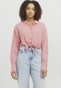 Rød og hvid stribet skjorte med knapper, bundet om livet, med lange ærmer og krave, parret med lyse højtaljede jeans.