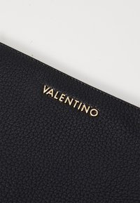 Fekete textúrált bőr clutch táska, amelyen arany "VALENTINO" embléma található a felső részen. Téglalap alakú, sima szélekkel.