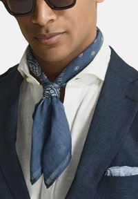 Sininen pellavahuivi valkoisilla kuvioilla, sidottuna kaulaan, yhdessä valkoisen paidan ja tumman bleiserin kanssa, jossa on taskuliina.