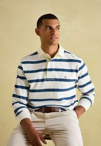 Biała i granatowa, w paski, koszulka polo z długim rękawem, z kołnierzykiem i haftowanym logo, zestawiona z kremowymi spodniami z kordurowej tkaniny i brązowym paskiem.