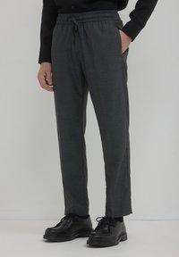 Pantalons gris fuselés en tissu texturé, avec une taille élastique et des poches latérales, associés à des chaussures noires à lacets.
