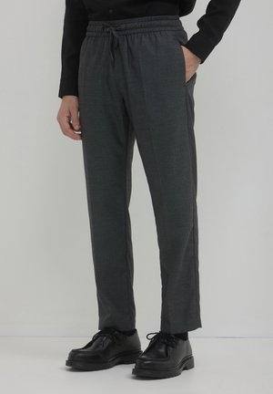 Graue taillierte Hose aus strukturiertem Stoff, mit elastischem Bund und Seitentaschen, kombiniert mit schwarzen Schnürschuhen.