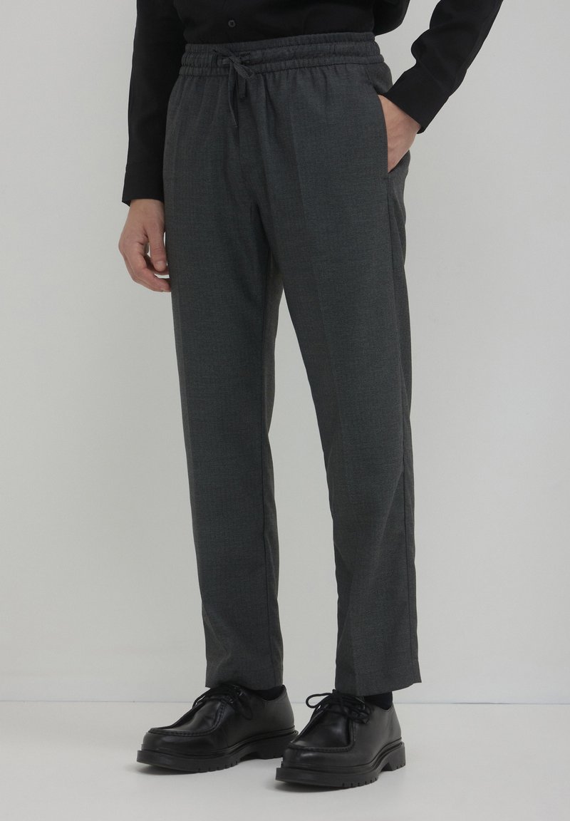 Pantalons gris fuselés en tissu texturé, avec une taille élastique et des poches latérales, associés à des chaussures noires à lacets.