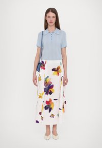 Lichtblauwe gebreide polo met korte mouwen, voorzien van een knoopsluiting. Witte rok versierd met kleurrijke bloempatronen. Puntige beige schoenen.