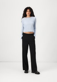 Lys blå ribbet langermet topp med cropped hem, kombinert med høy midje sorte bukser og svarte sko mot en enkel hvit bakgrunn.