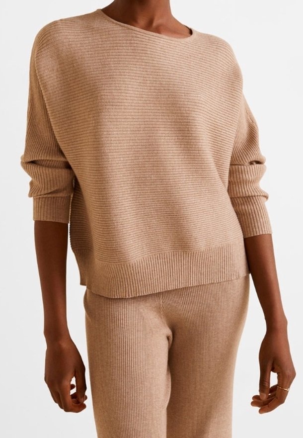 Personne portant un pull en tricot côtelé beige et un pantalon assorti en tricot côtelé avec des manches longues et une coupe décontractée.