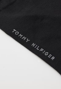 Fekete textil, amelyen szürke színben van woven "TOMMY HILFIGER" logó. Az anyag simának tűnik, enyhén texturált felülettel.