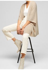 Cardigan in maglina beige con motivo testurizzato, tessuto leggero, apertura frontale e maniche larghe, abbinato a pantaloni cropped color crema e stivali leggeri.