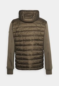Polstret olivgrøn jakke med hætte, der har quiltet tekstur på den øverste del og tætsiddende ærmer i et kontrasterende mat stof.