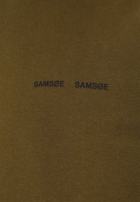 T-shirt en tissu tricoté vert olive avec deux noms de marque brodés en noir "SAMSOE" affichés horizontalement. Texture lisse avec un design ajusté.