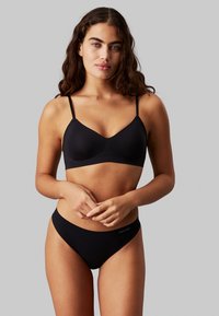 Black bra and matching bikini briefs made of smooth fabric. The bra features adjustable straps and a simple design, with a logo on the waistband.