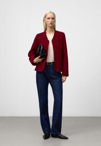 Bordowa wełniana kurtka z czarnymi guzikami, zestawiona z jasnym topem, ciemnymi dżinsami i małą czarną torebką. Czarne, spiczaste buty.