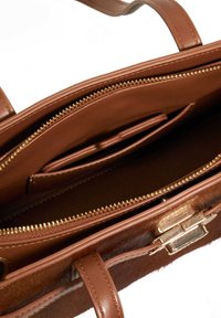Tan leather handbag with zippered compartments, smooth and textured surfaces, gold hardware, interior pockets, and a structured design.