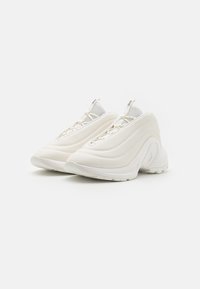 Baskets de sport blanches avec une tige synthétique lisse, des accents en mesh, un bout arrondi et une semelle texturée. Présente un design de talon incurvé et un système de laçage.