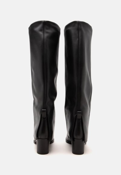 Paire de longues bottes en cuir noir avec talons blocs, vues de dos sur un fond neutre.