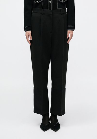 Pantalon noir taille haute à jambes larges, avec des plis et une finition texturée. Conçu avec un détail de revers plié à l'ourlet.