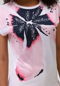 Kortermet, hvit t-skjorte med et stort blomstermotiv i rosa og marineblått med svarte detaljer og vanndråpeeffekter.