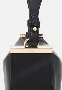 Schwarze Lederhandtasche mit strukturierter Form, goldenen Hardware-Akzenten, einem dicken Riemen und sichtbaren Nähdetails. Das Markenlogo ist geprägt.