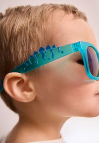 Aqua-blaue Sonnenbrille mit einem strukturierten Rahmen, der ein stacheliges Design an den Seiten aufweist, und reflektierenden Gläsern.
