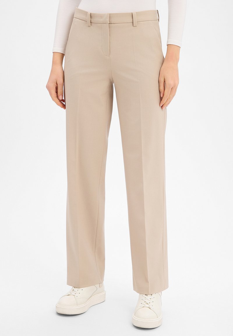 Beige Hose mit geradem Bein, kombiniert mit weißen Sneakern und einem weißen Langarmshirt, dargestellt von der Taille bis zu den Füßen.