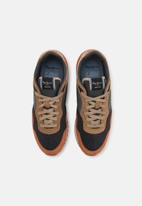 Zapatillas con parte superior de malla negra, detalles en ante marrón, cordones beiges y suela de goma blanca; presenta logotipos en la lengüeta y el lateral.