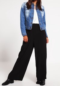 Džínová bunda v světle modré barvě s přiléhavým střihem, spárovaná s volnými černými kalhotami s širokými nohavicemi. Černé kotníkové boty dotvářejí celkový outfit.