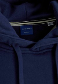 Marineblauwe hoodie met een trekkoord, zachte textuur en een label met "JACK & JONES" branding. Aan de binnenkant heeft het een halslijn met witte streepdetaillering.