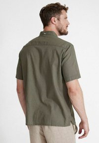 Camicetta verde scuro a maniche corte realizzata in tessuto leggero, con colletto a bottoni e orlo dritto con spacchetti laterali.