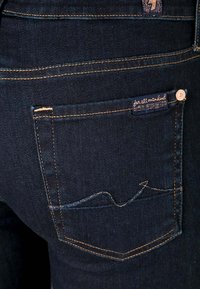 Los jeans de mezclilla azul oscuro presentan un bolsillo trasero con un patrón de costura curvo y una etiqueta que dice "para toda la humanidad".