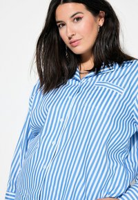 Camisa de botones a rayas azul y blanca con un bolsillo en el pecho, mangas largas y cuello con muesca, fabricada en un tejido ligero.