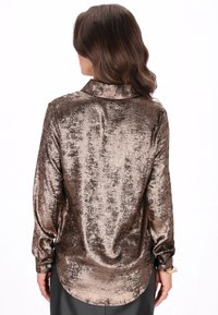 Kiiltävä ruskea metallinhohtoinen paita, jossa on kaulus, pitkät hihat ja napilliset kalvosimet; siinä on tekstuuri kangas hienovaraisella kiillolla ja suora helma.