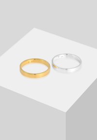 Dos anillos minimalistas, uno en oro pulido y otro en plata pulida, ambos con bandas redondas y suaves con un acabado reflectante.