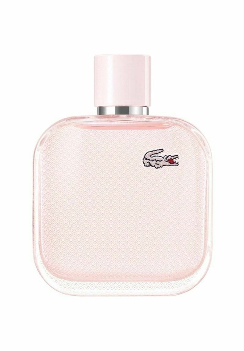 Neliön muotoinen vaaleanpunainen lasinen parfyymipullo, jossa on teksturoitu pinta ja hopeiset yksityiskohdat; sisältää pienen kirjontakrokotiililogon.