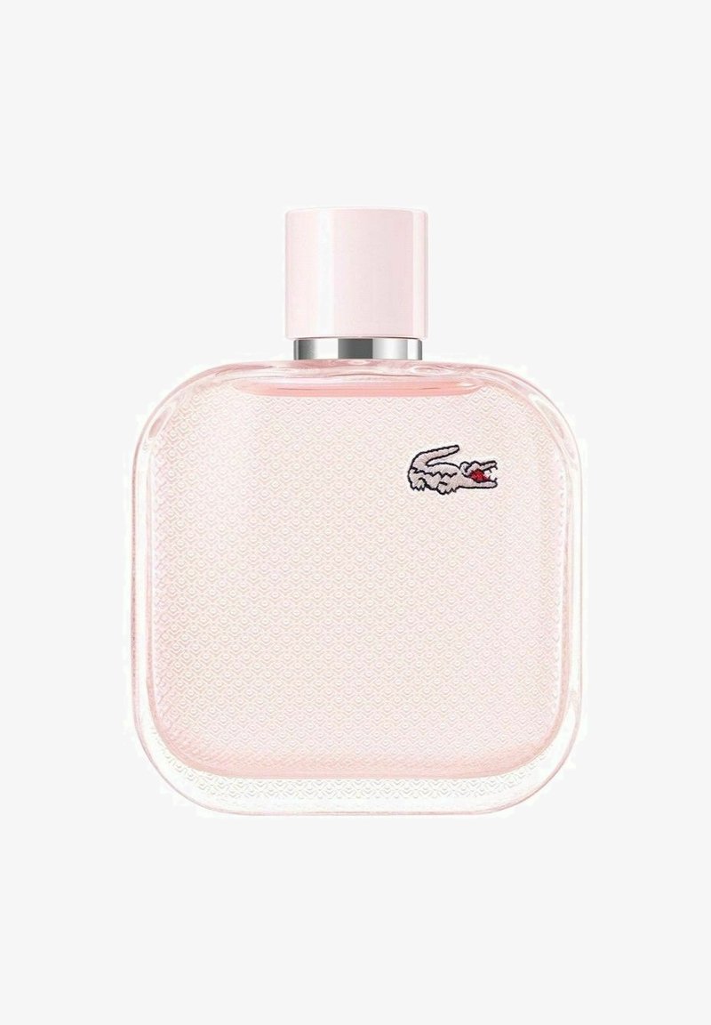 Neliön muotoinen vaaleanpunainen lasinen parfyymipullo, jossa on teksturoitu pinta ja hopeiset yksityiskohdat; sisältää pienen kirjontakrokotiililogon.