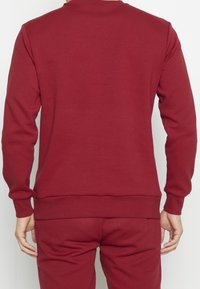 Bordeaux bluza z miękkiej dzianiny bawełnianej, z okrągłym dekoltem, ściągaczami przy mankietach i u dołu, o gładkiej teksturze i minimalistycznym wzornictwie.